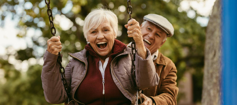 Senior man pushing his female partner on swing in park and having fun together.